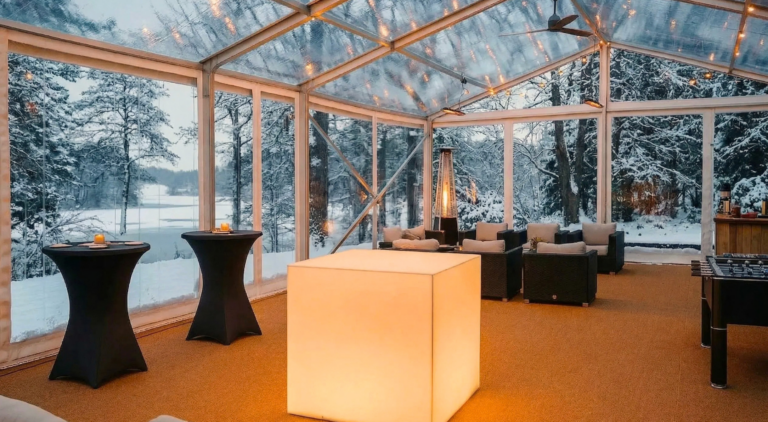 Glasat tält med levande ljus och loungemöbler i snölandskap vid havet på Villa Sandudden